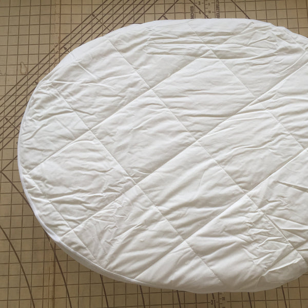 Round white quilted pad on a grid background